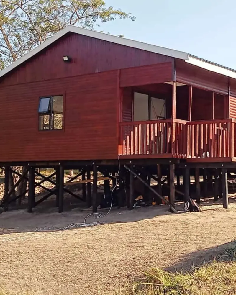 Red-brown timber log home with a covered deck, raised on wooden stilts