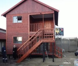 Double-storey wooden log home with external staircase by Mutsamvi Construction.